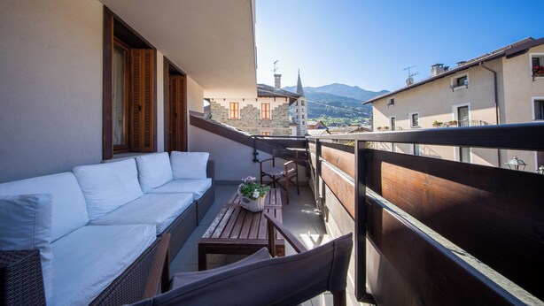 A balcony with a white sofa, wicker furniture, and a table with a basket of flowers.