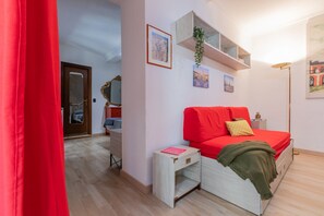 A bedroom with a red sofa, a small bedside table, a mirror, and a shelf with pictures. - Giolitti San Carlo Stay by Wonderful Italy (Turin)