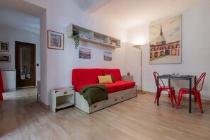 Ein kompakter Wohnraum mit einem roten Sofa, einem kleinen Esstisch mit roten Stühlen und einem Wandregal mit Dekoration.