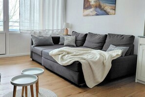A modern living room with a grey sofa, white throw blanket, and two small white side tables. - Cozy Apartment with Stunning Views in Marina Wendtorf (Wendtorf)