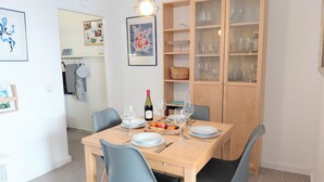 A dining area with a wooden table set for four, chairs, a wine bottle, and a fruit bowl. - Cozy Apartment with Stunning Views in Marina Wendtorf (Wendtorf)