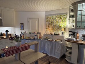 Une cuisine avec un coin repas, comprenant une table recouverte d’une nappe à carreaux rouges et blancs, un banc et une bougie. On y trouve divers appareils de cuisine et ustensiles sur les plans de travail.
