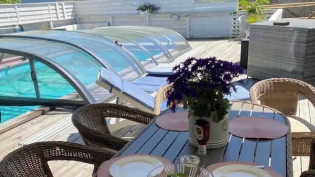 Un coin repas avec des chaises en osier, une table ronde et une vue sur une piscine.