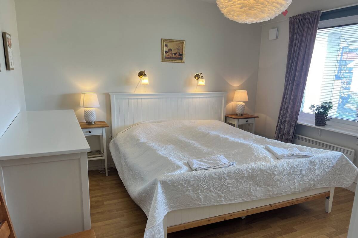 Un dormitorio ordenado con una cama, mesitas de noche y un ventanal con cortinas.