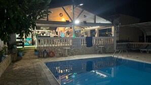 Une piscine avec une terrasse en pierre, un coin bar avec des chaises et un espace de détente au bord de la piscine.