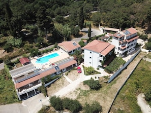 An aerial view of a residential area with a swimming pool, multiple buildings, and surrounding greenery.
