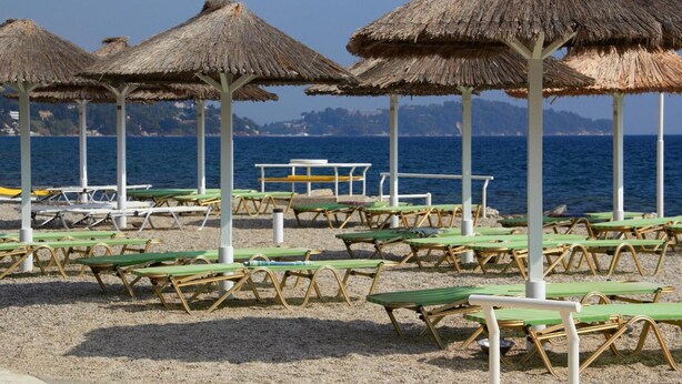 Une plage avec des parasols en chaume et des chaises longues vertes.