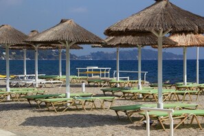 A beach with thatched umbrellas and green lounge chairs.