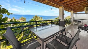 Un espace extérieur abrité, doté d’une table et de chaises, offrant une vue panoramique sur la mer et la verdure.