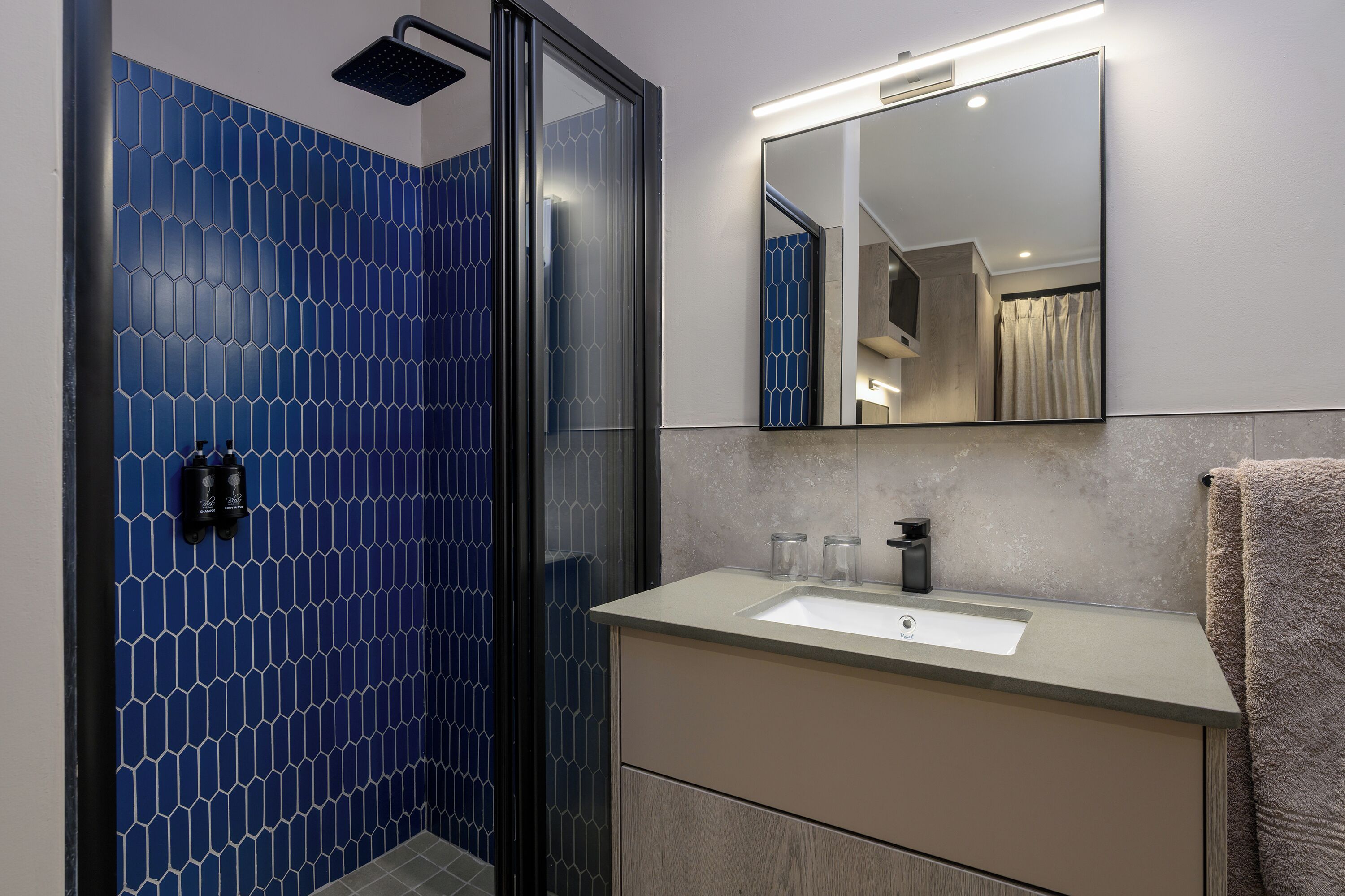Une salle de bain avec un mur recouvert de carreaux hexagonaux bleus, une douche en verre, un lavabo avec un miroir et un porte-serviettes.
