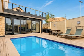 A modern building with a pool, outdoor seating, and a covered patio area.