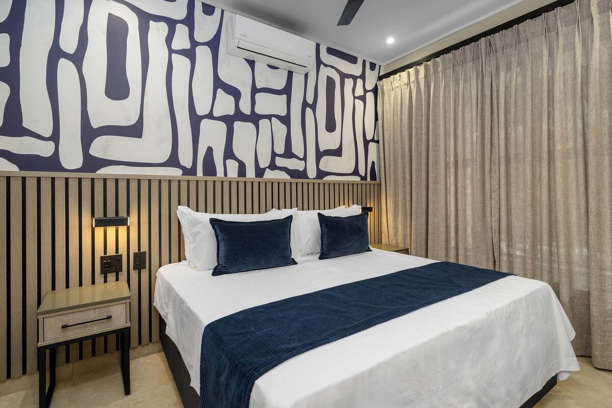A modern hotel room with a large bed, a nightstand, a wall-mounted air conditioner, and a curtain.