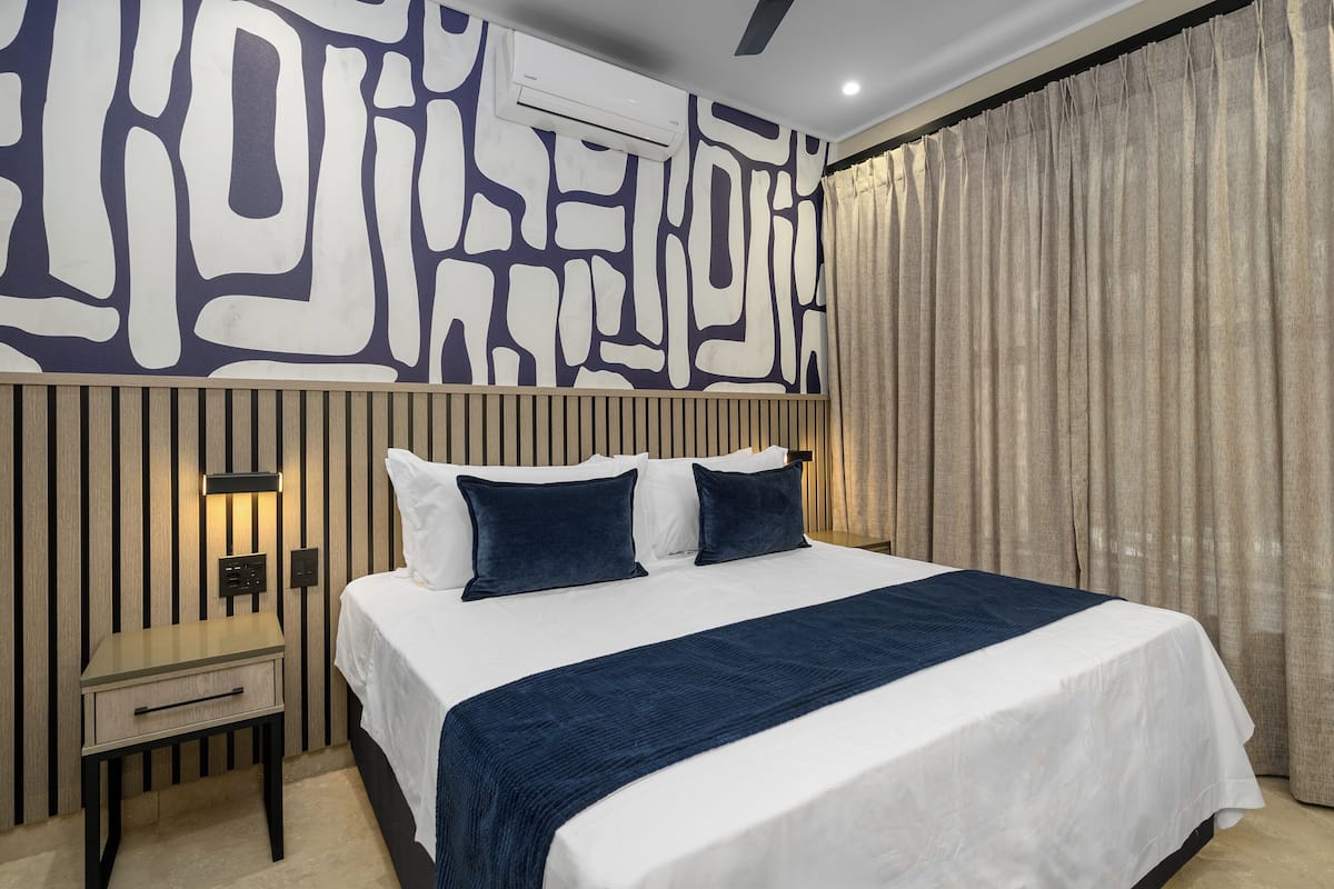 A modern hotel room with a large bed, a nightstand, a wall-mounted air conditioner, and a curtain.