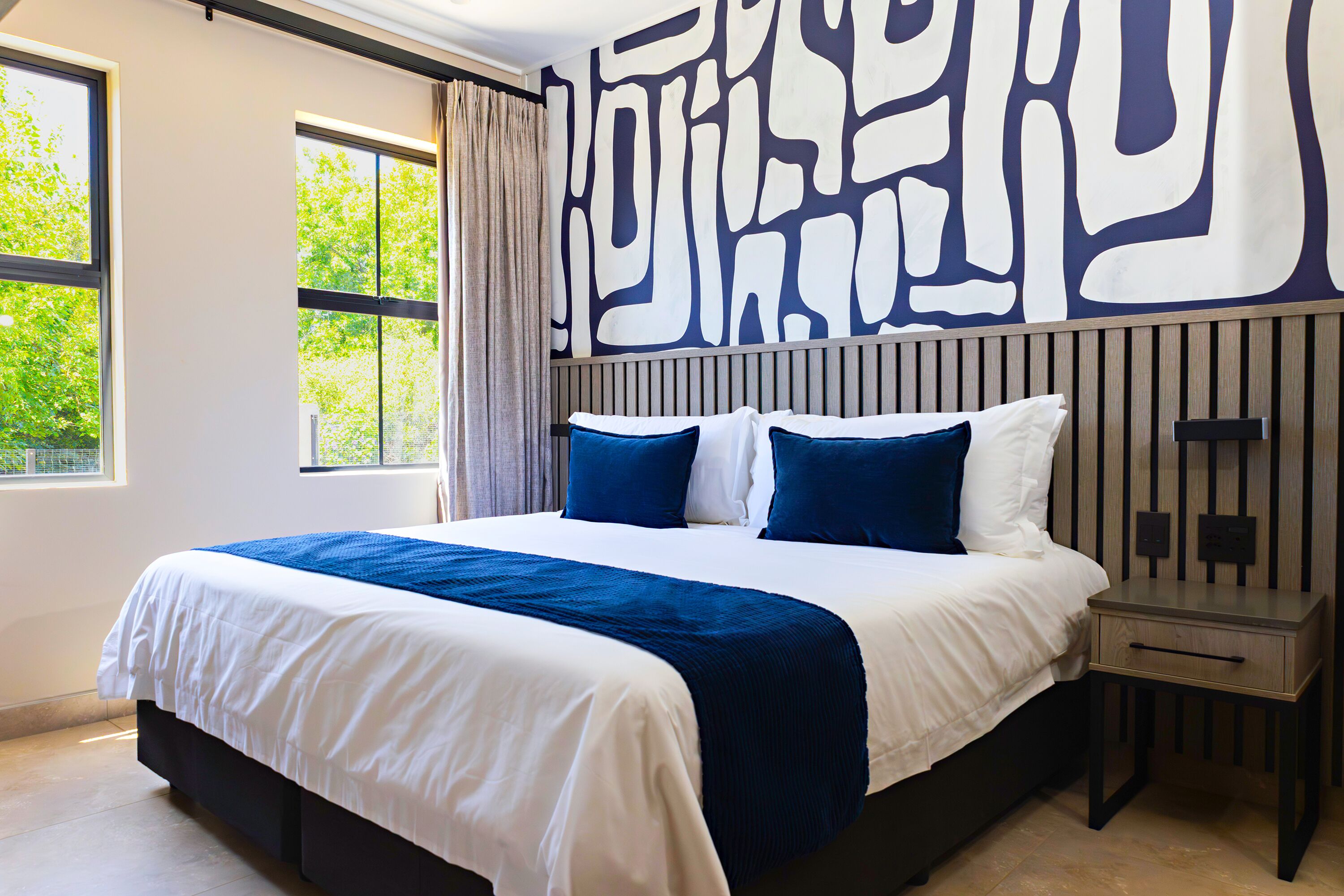 A modern hotel room with a large bed, a nightstand, and a wall with abstract art.