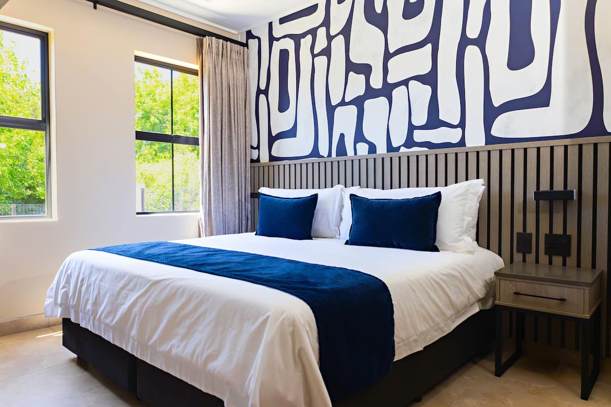 A modern hotel room with a large bed, a nightstand, and a wall with abstract art.