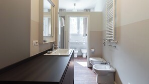 Ein modernes Badezimmer mit dunkler Ablage, einem Spiegel, einem Bidet und einer Toilette.