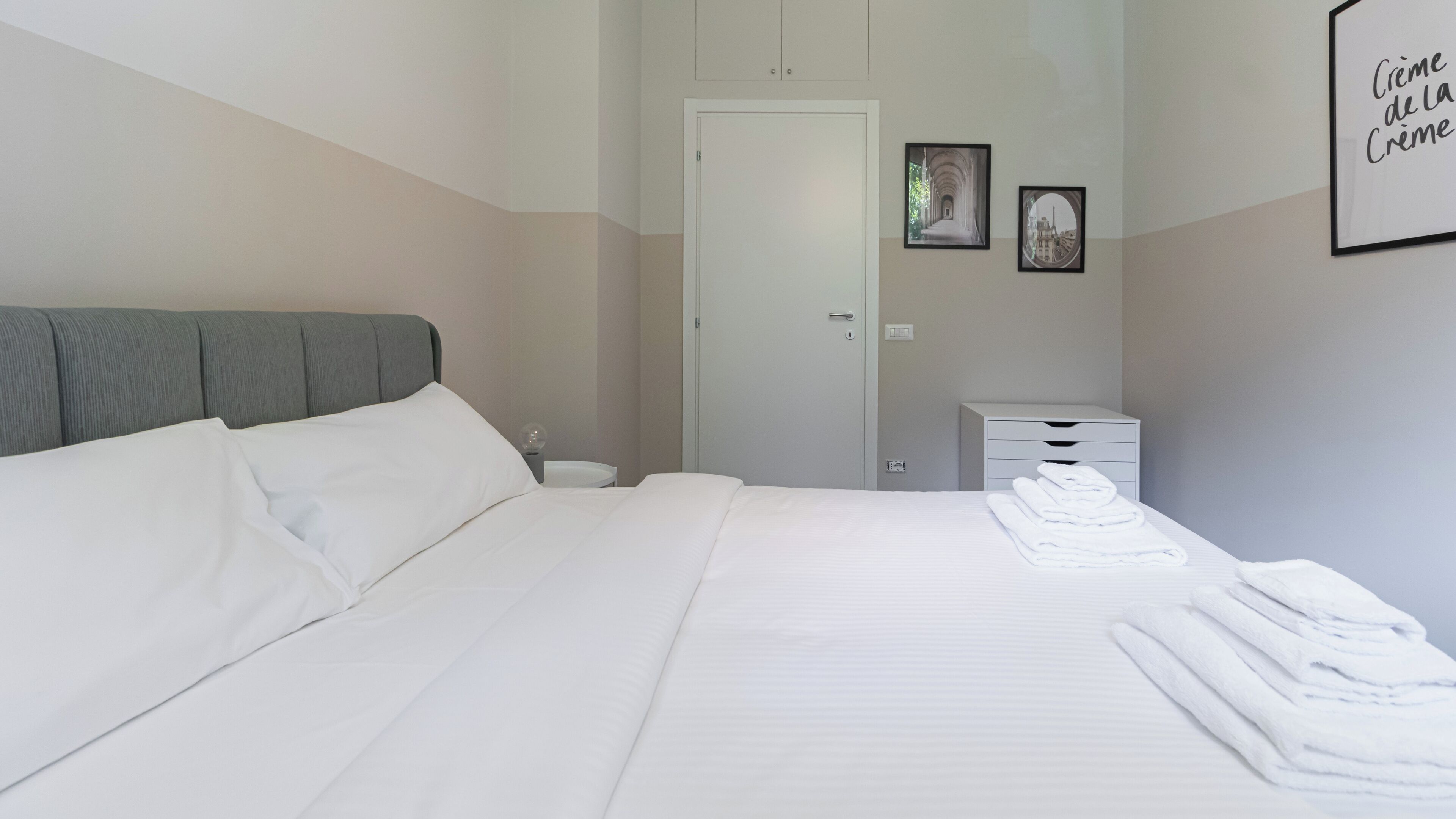 A hotel room with a bed, a bedside table with a lamp, a wardrobe, and a framed picture on the wall.
