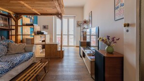 Ett mysigt vardagsrum med ett träpanelat tak, en soffa, ett soffbord och en tv. Det finns en bokhylla och en dörr som leder till ett annat rum.