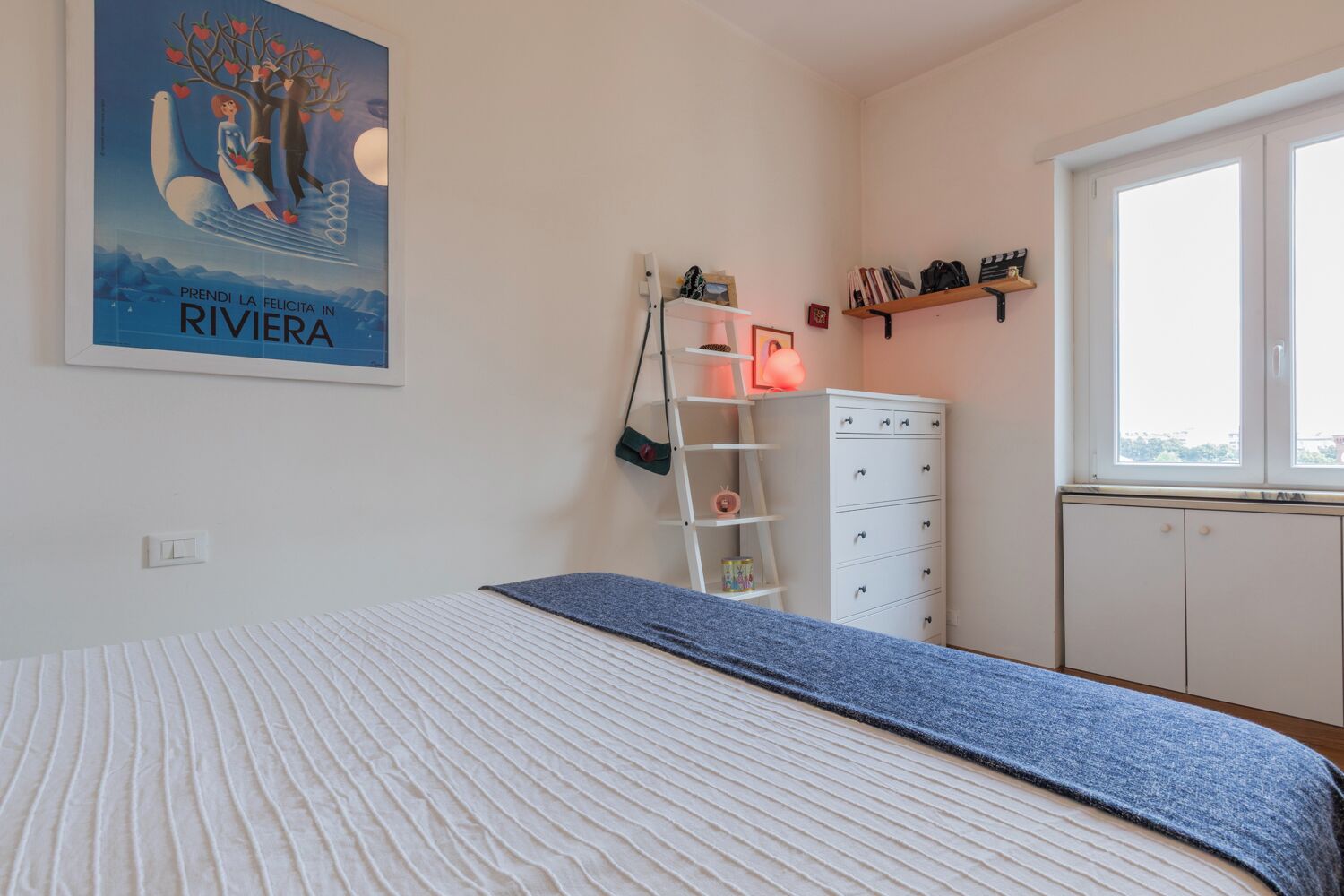 A bedroom with a bed, a dresser, a ladder, and a window.