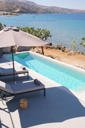 A poolside area with a lounge chair, umbrella, and a small wooden stool. - Floating Cubes Villa Aegina, Floating Cubes Villas Aegina (Aegina)