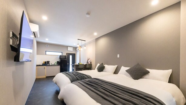 Une chambre d’hôtel avec deux lits, une kitchenette et un téléviseur fixé au mur.