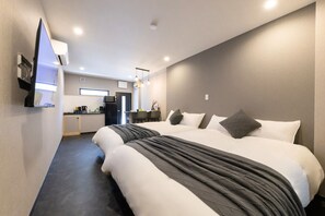 Habitación de hotel con dos camas, kitchenette y televisión montada en la pared.