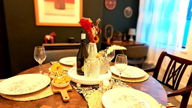 A dining table set with plates, glasses, a bottle, and a vase with dried flowers. - Cosy Stay in Coventry CV5 | King Bed & Twin Room | Free Parking | Sleeps 4 (Coventry)