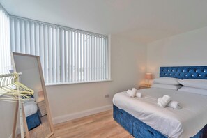 A bedroom with a bed, a bedside table, a lamp, a mirror, and a window with blinds. - Contemporary & Bright 1 Bed Apartment in Gravesend (Gravesend)