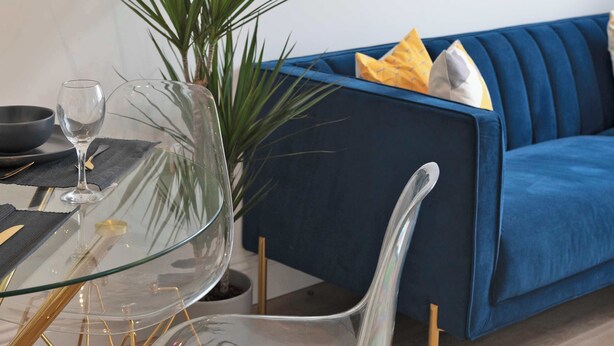 A modern living room with a glass table, a blue sofa, and a potted plant. - Contemporary & Bright 1 Bed Apartment in Gravesend (Gravesend)