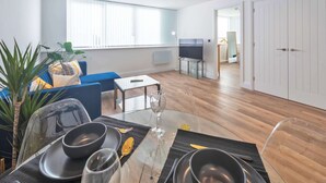 A modern living room with a dining area, wooden flooring, a large window, and a TV. - Contemporary & Bright 1 Bed Apartment in Gravesend (Gravesend)