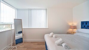 A hotel room with a bed, a bedside lamp, a mirror, and a window with blinds. - Contemporary & Bright 1 Bed Apartment in Gravesend (Gravesend)