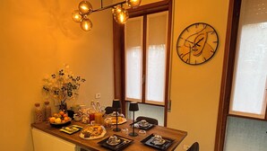 Un coin repas avec une table en bois, deux chaises, une horloge au mur et une fenêtre avec des stores.