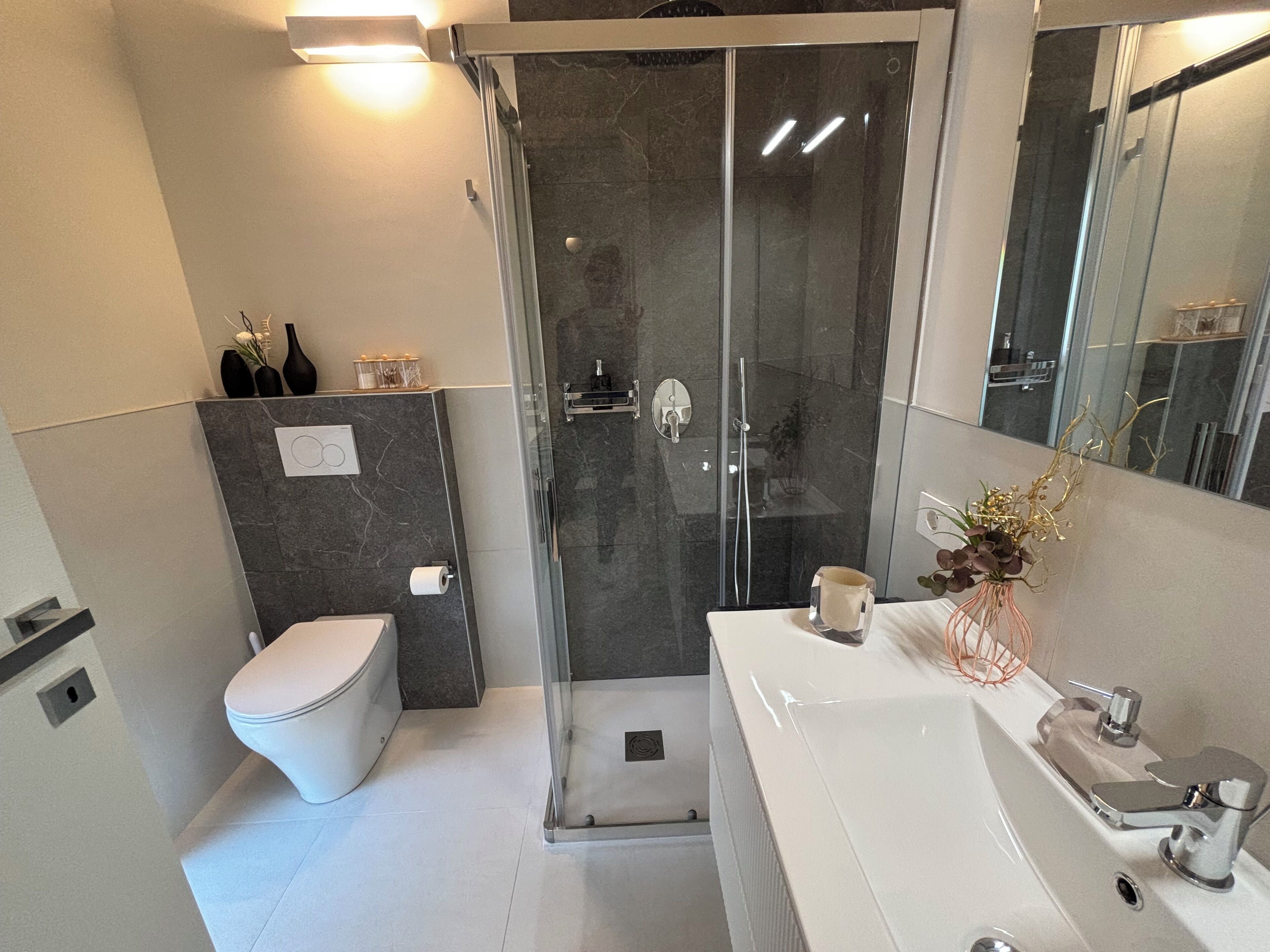 A modern bathroom with a glass-enclosed shower, a white toilet, and a vanity with a mirror.