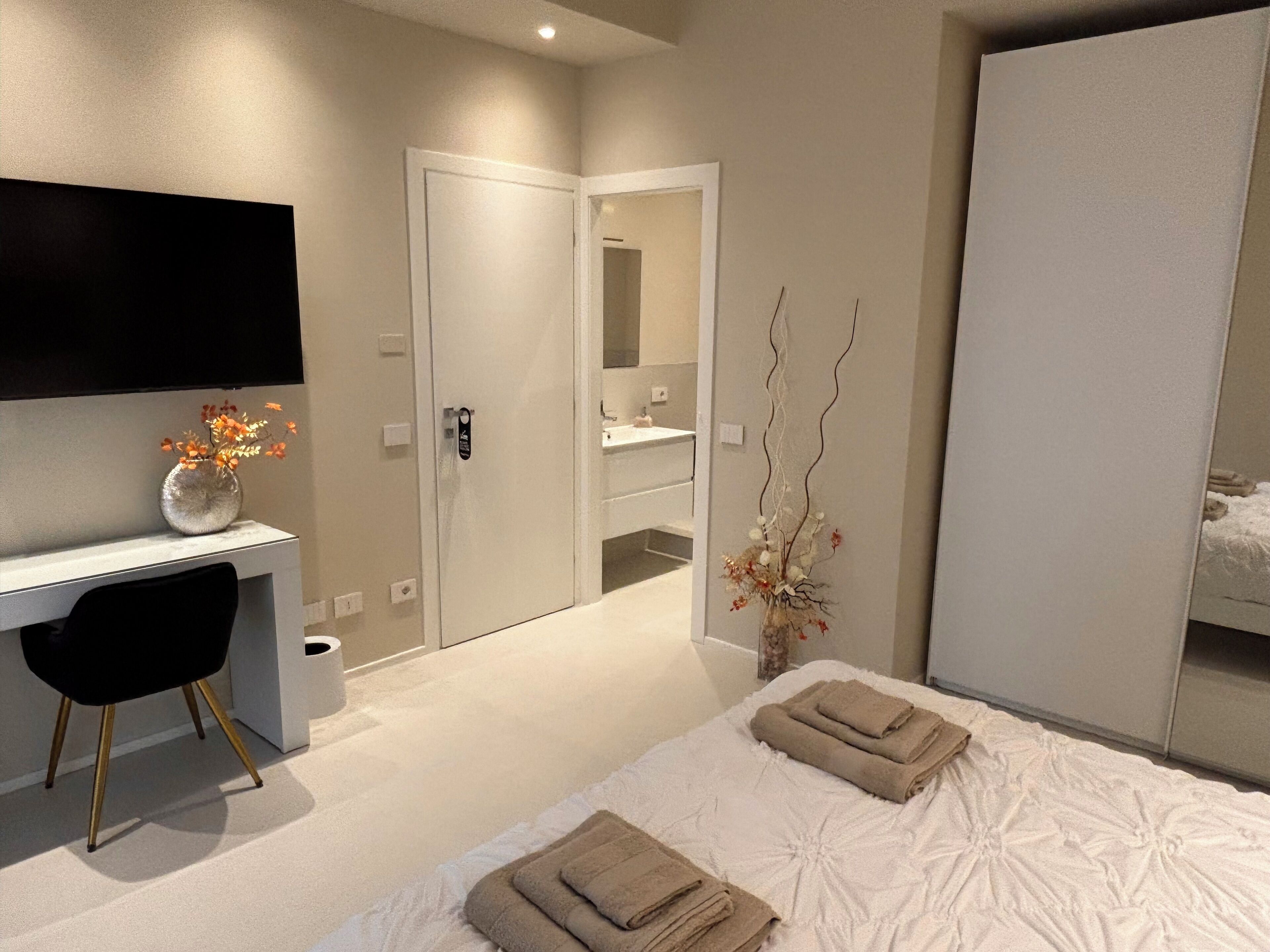 A modern hotel room with a bed, a desk, a chair, and a large mirror.