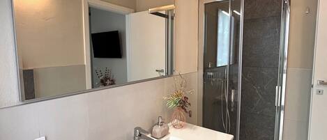 Een moderne badkamer met een wit badkamermeubel, een grote spiegel, een douchecabine van glas en een ingebouwde radiator.