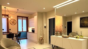 Un salon moderne comprenant un canapé, un coin repas avec des chaises, une console blanche agrémentée d’objets décoratifs et une horloge murale.