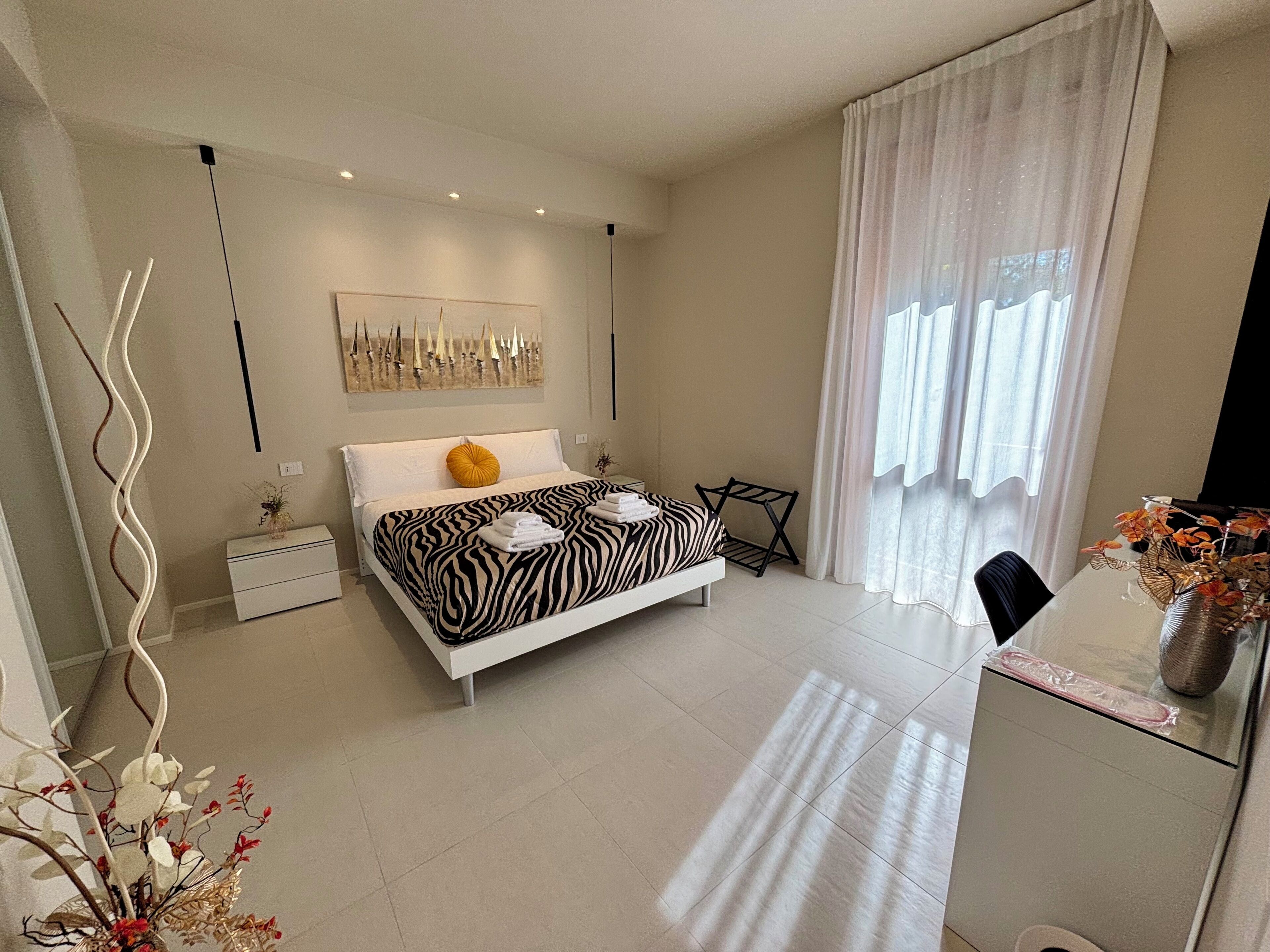 A modern bedroom with a zebra-patterned bedspread, a single yellow pillow, and neatly folded towels on the bed.