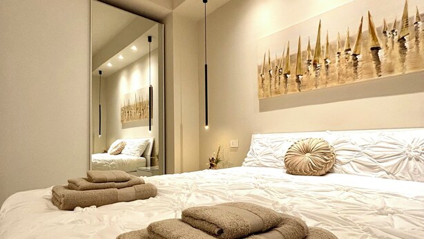 Une chambre moderne avec un grand lit, un miroir et une œuvre d’art accrochée au mur.