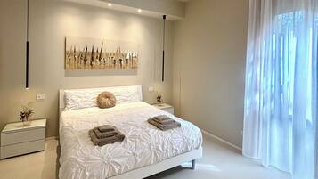 Una camera da letto moderna con un letto grande, comodini, un'opera d'arte appesa al muro e un'ampia finestra con tende leggere.