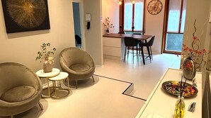 Un salon moderne avec deux fauteuils, une petite table et un coin repas agrémenté d’un lustre.