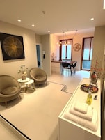 Una sala de estar moderna con dos sillones, una mesita y un comedor con candelabro.