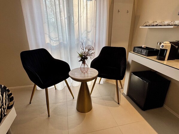 A small, modern kitchen with two black chairs around a round table, a coffee bar, and a refrigerator.