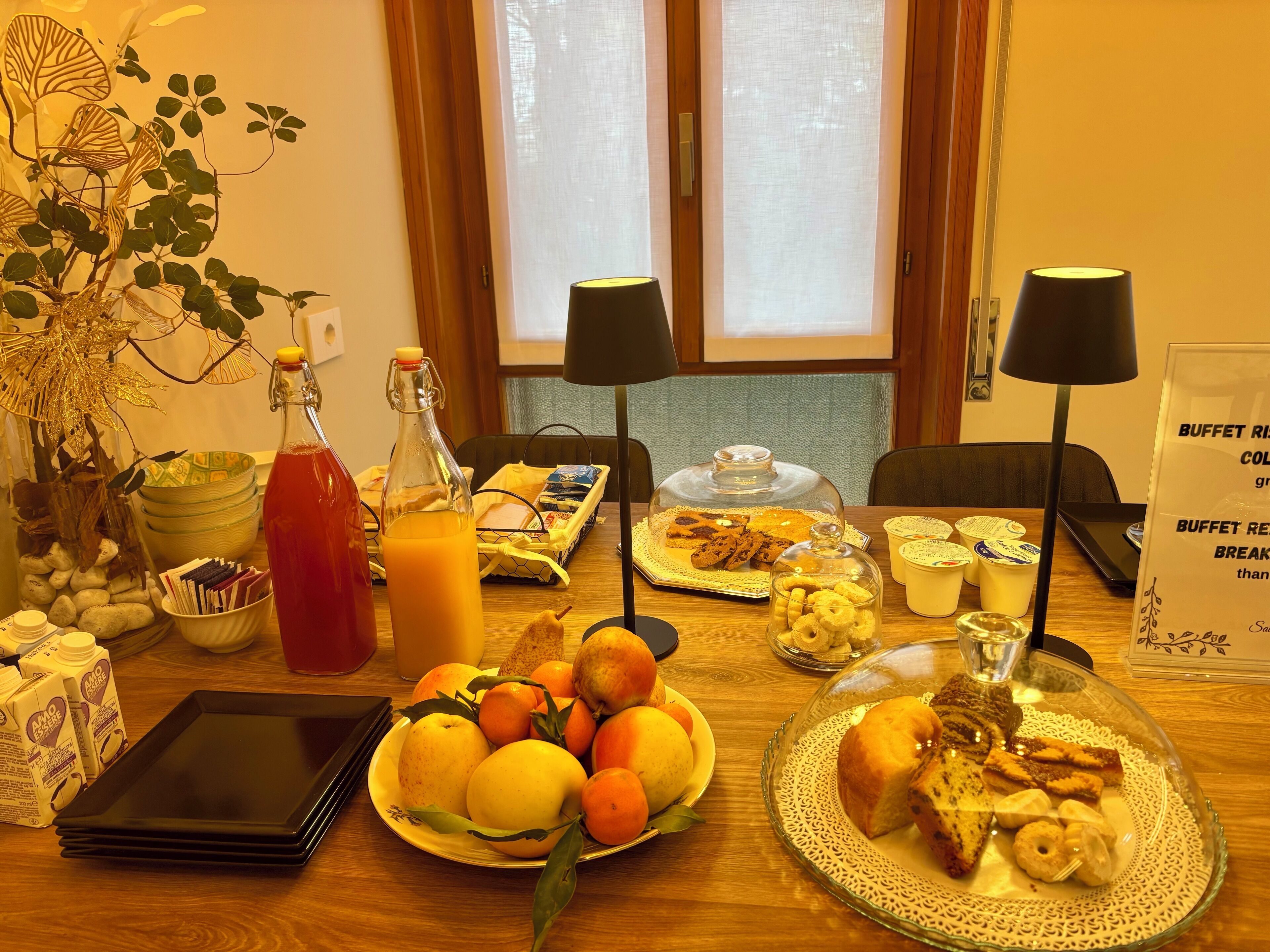 A breakfast table with fruits, pastries, and beverages, a tablet, and a buffet sign.