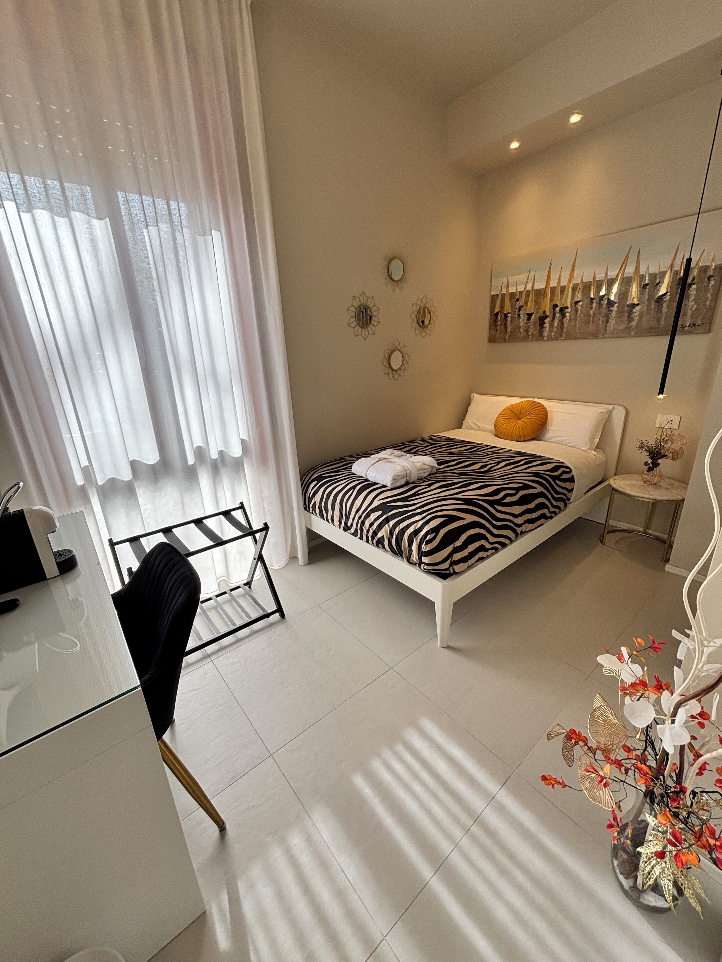 Un dormitorio moderno con una cama estampada con motivos de cebra, un escritorio blanco y una silla de cristal.