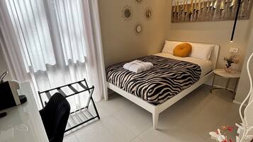 Un dormitorio moderno con una cama estampada con motivos de cebra, un escritorio blanco y una silla de cristal.