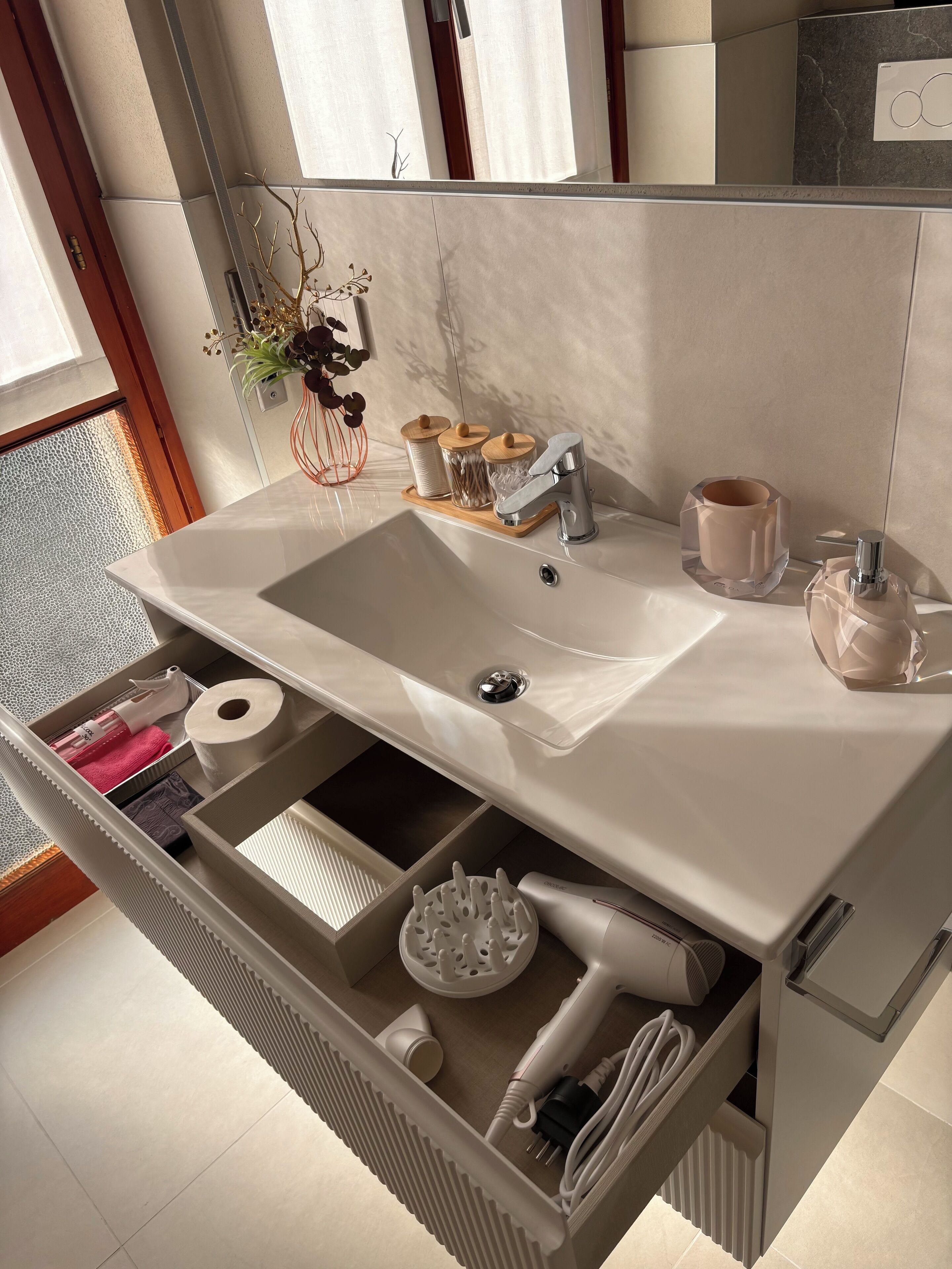 A modern bathroom with a white sink, a mirror, and a built-in storage drawer.