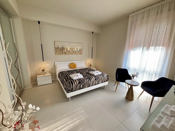 Une chambre moderne avec un lit à motifs zébrés, une petite table ronde, deux chaises et un élément décoratif mural.