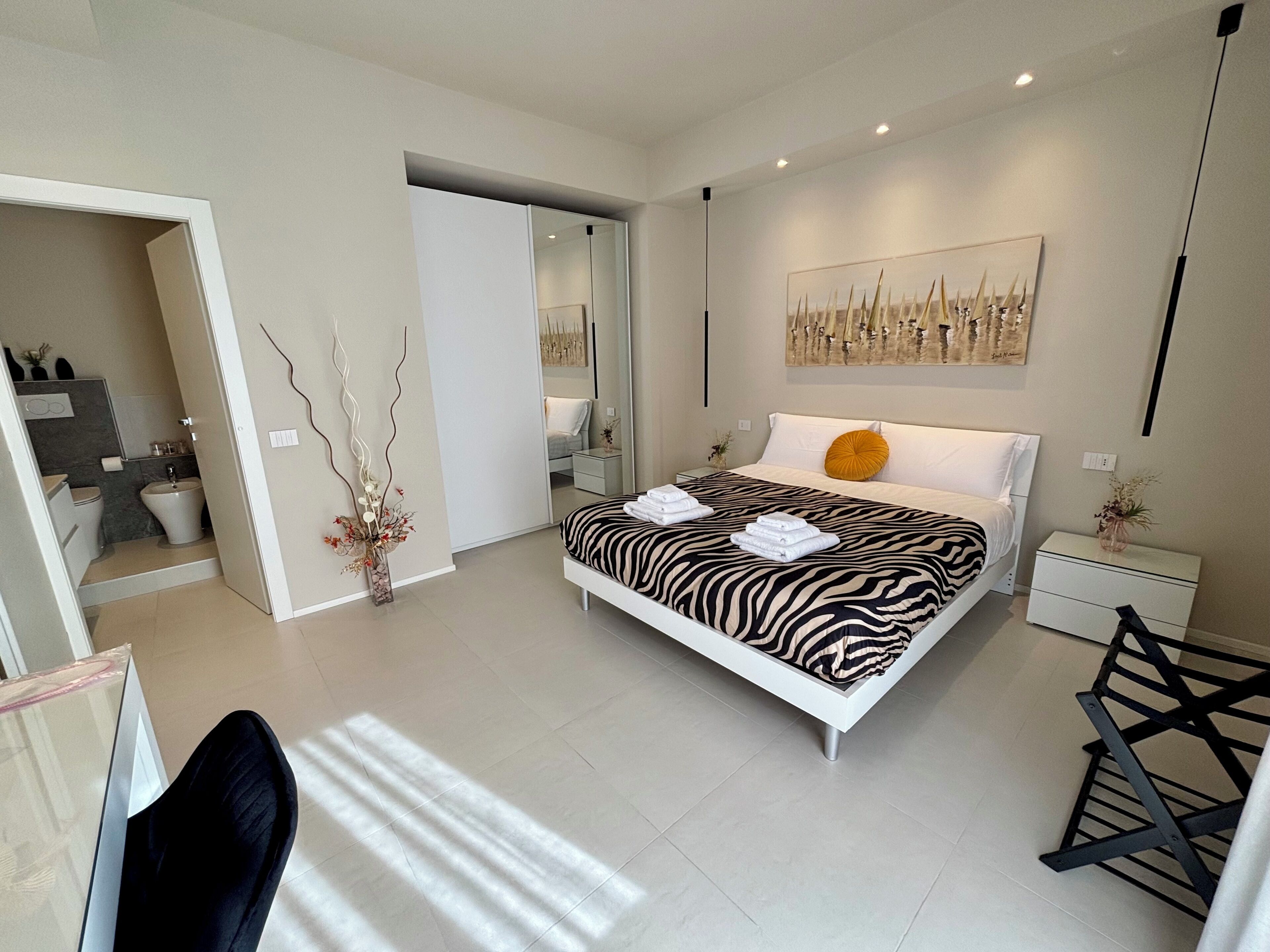 A modern bedroom with a zebra-patterned bed, a bedside table, a nightstand, a chair, and a large mirror.