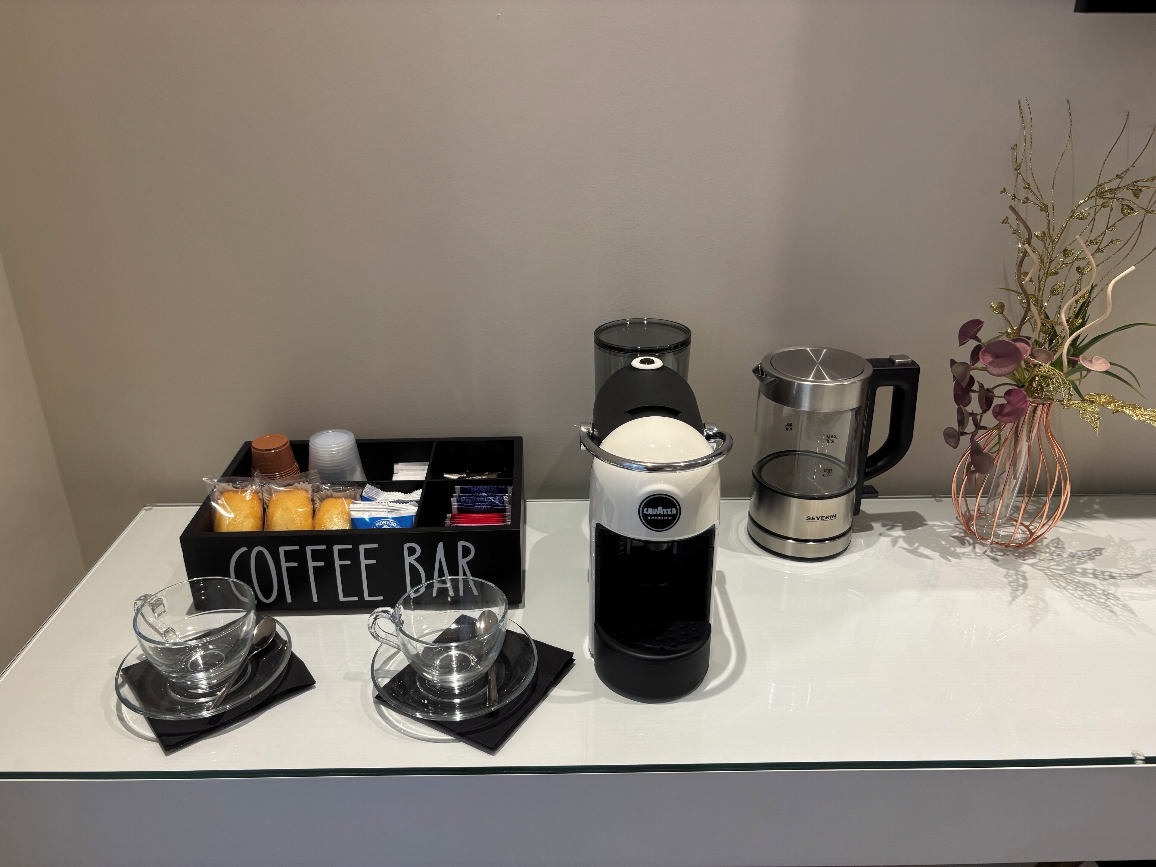 Una barra de café con una cafetera, una jarra de café y una caja con la etiqueta 'COFFEE BAR'.
