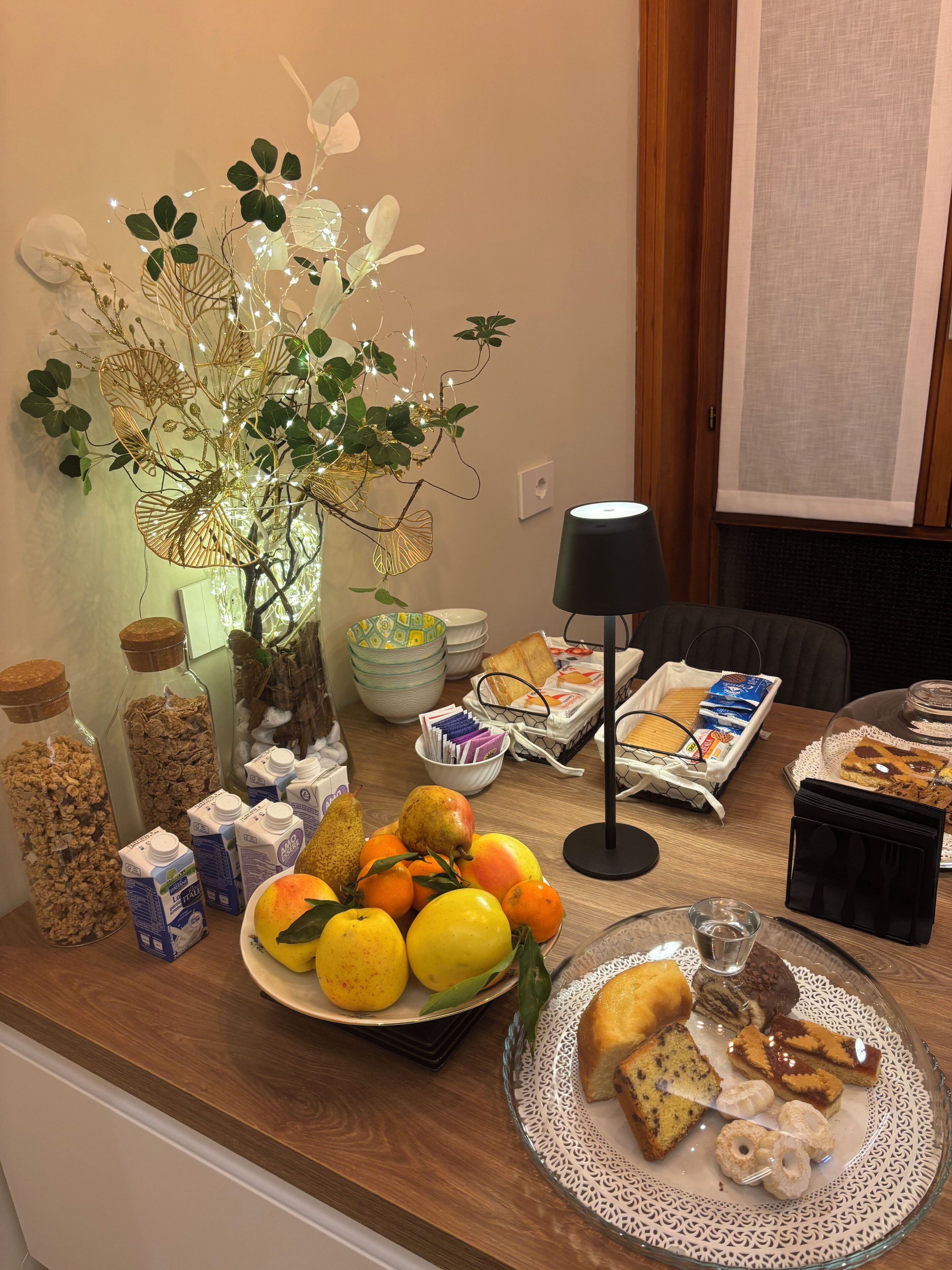 A breakfast buffet with various food items, a decorative plant, and breakfast essentials on a wooden table.